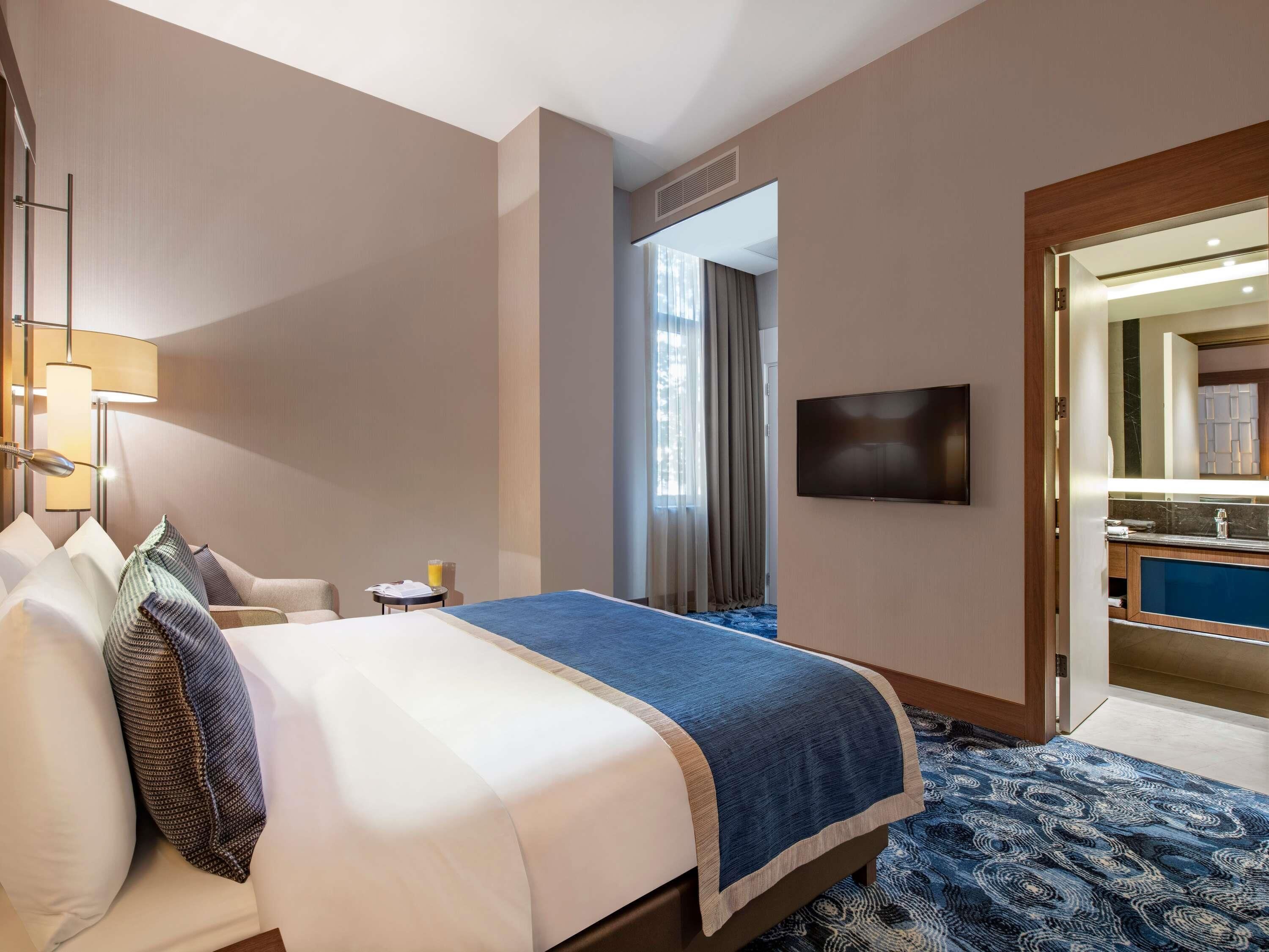 Une chambre d’hôtel avec un lit, un bureau, une chaise, une télévision et une salle de bain visible à travers une porte ouverte.