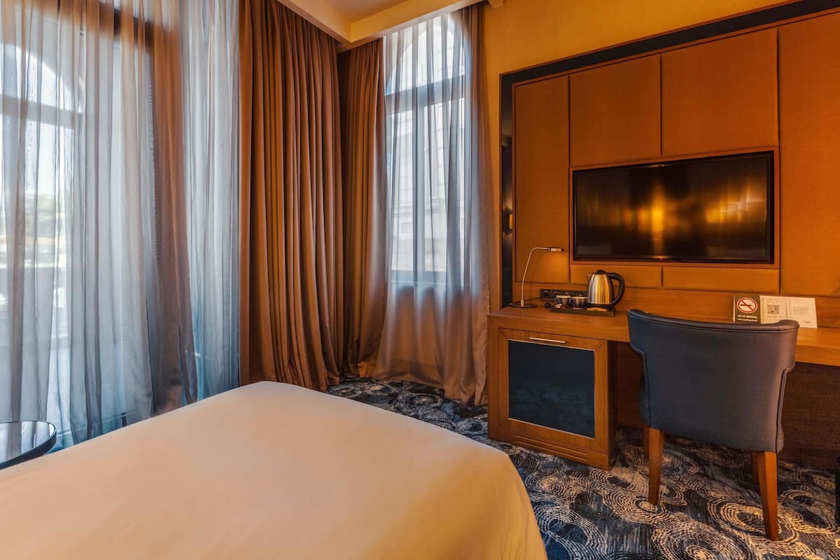 Ein Hotelzimmer mit einem Bett, einem Schreibtisch mit Fernseher, einem Sessel und einer Kaffeemaschine.