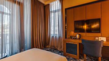 A hotel room with a bed, a desk with a television, a chair, and a coffee maker.