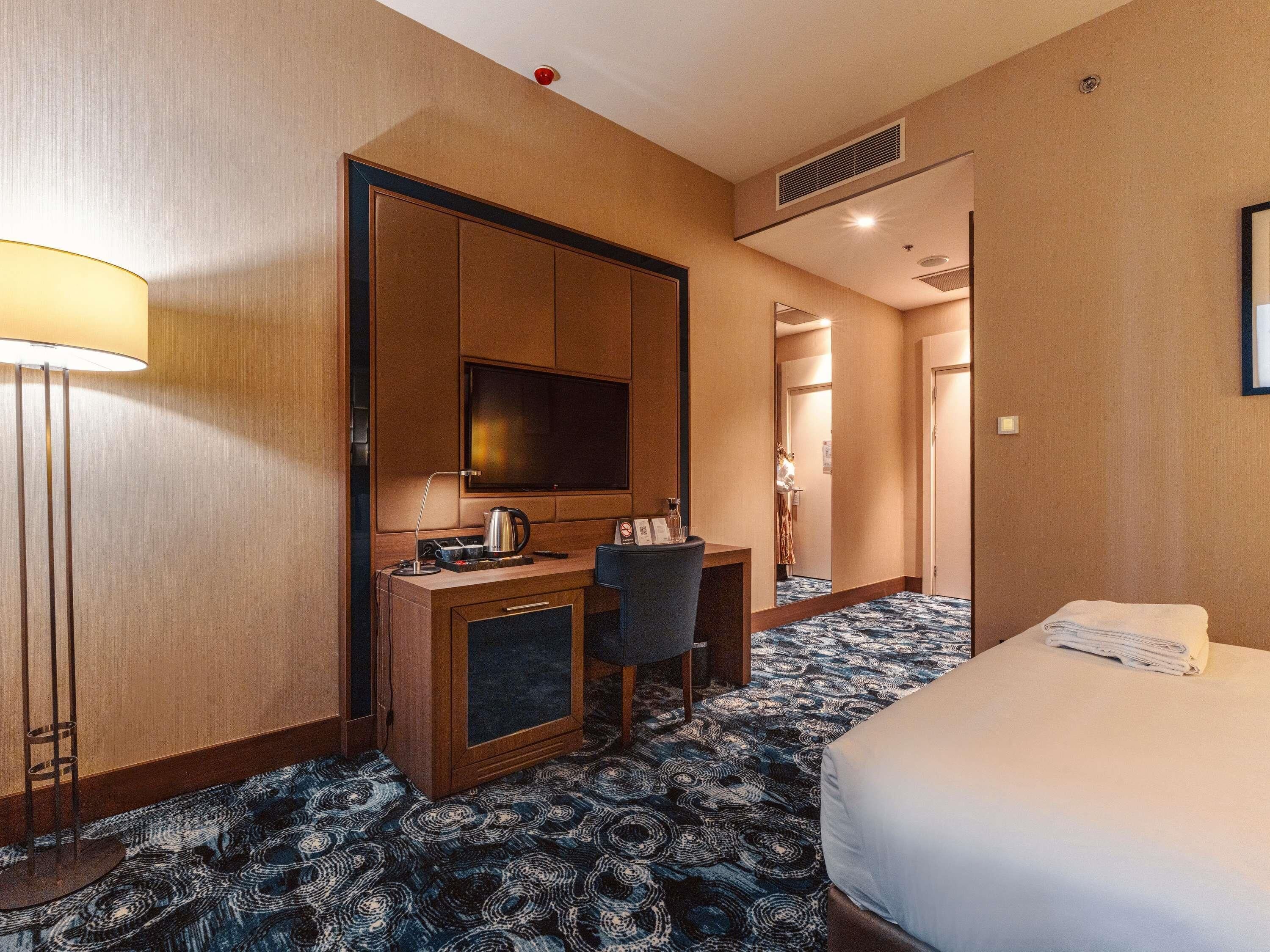 Une chambre d’hôtel avec un lit, un bureau doté d’une télévision, une lampe et une moquette à motifs.