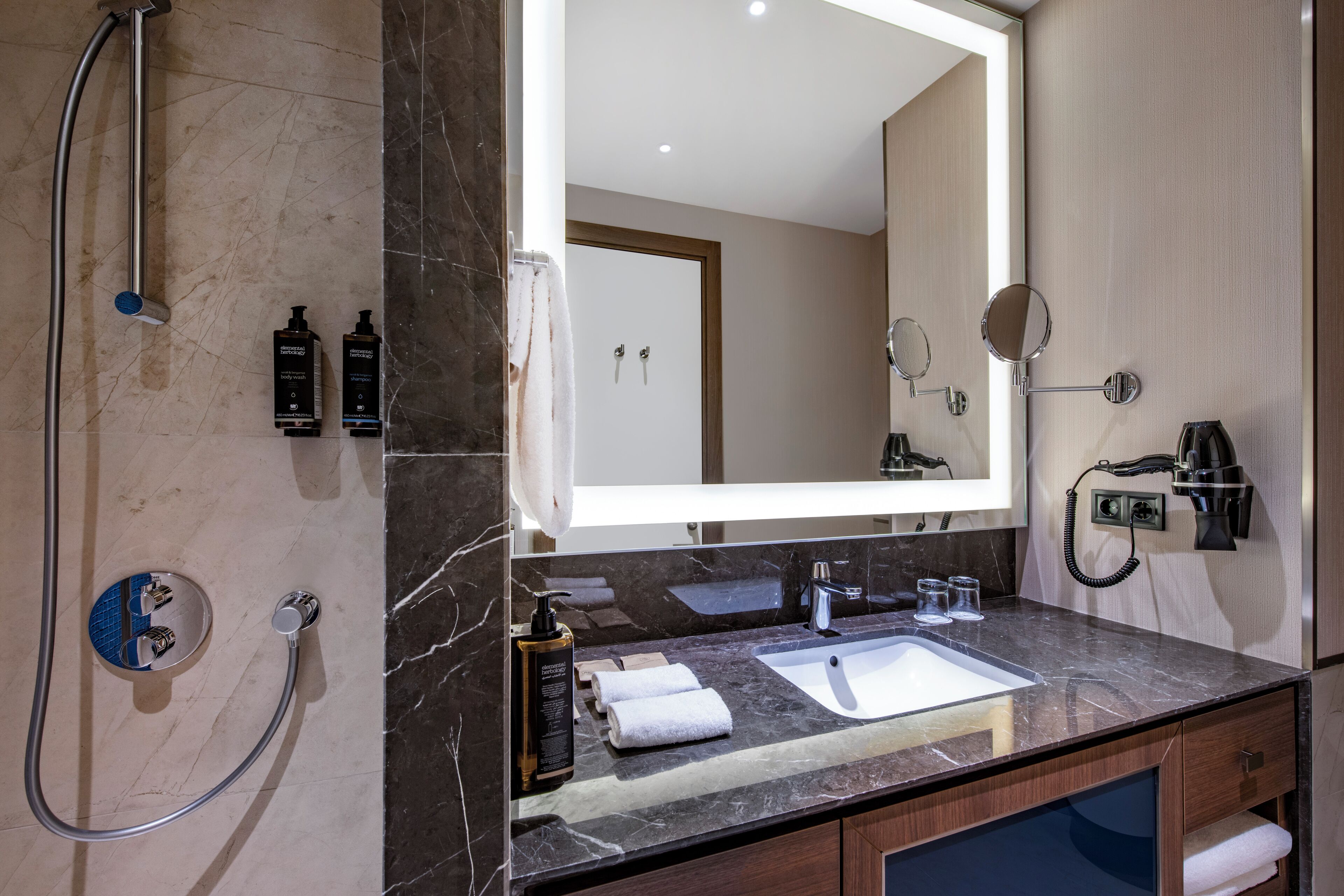 A modern bathroom with a large mirror, dual sinks, a shower, and a hairdryer.