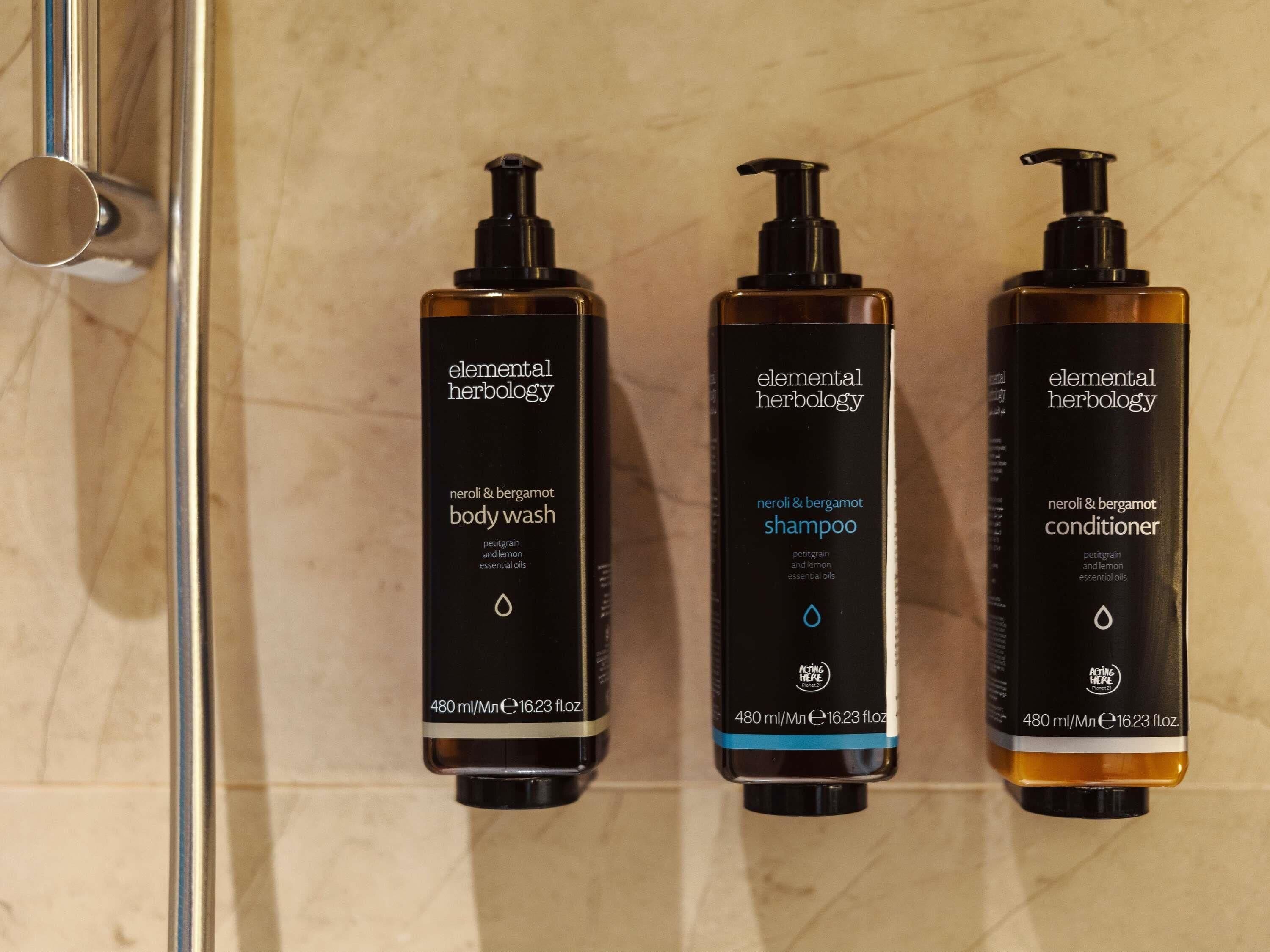 Tre flaskor med produkter från varumärket Elemental Herbology: duschkräm, schampo och balsam, alla med en pumpflaska och en liten droppsymbol.