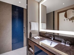 Un baño moderno con un lavabo de mármol, un espejo grande y una zona de ducha con azulejos azules.