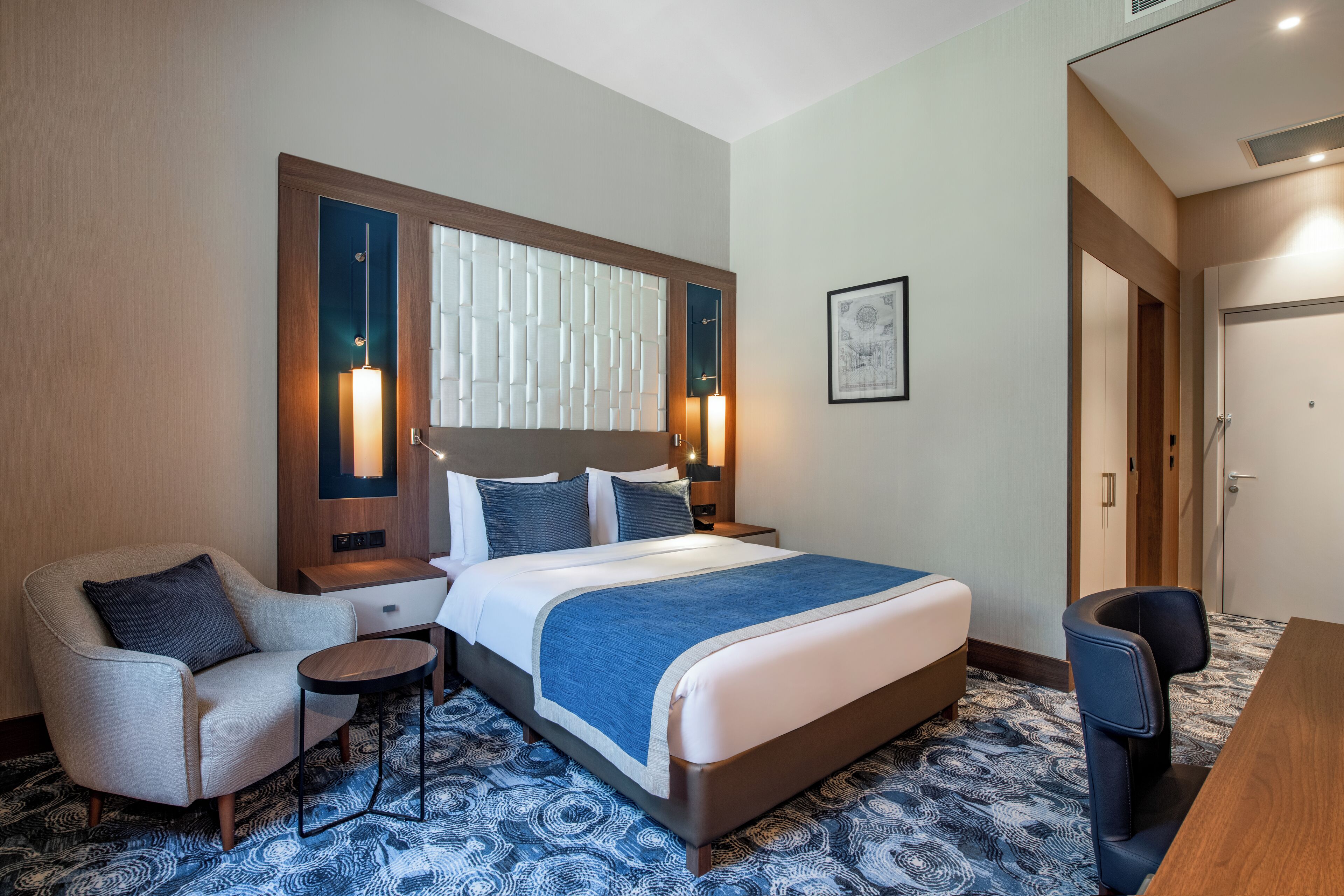 A hotel room with a large bed, a desk, a chair, and a small table.