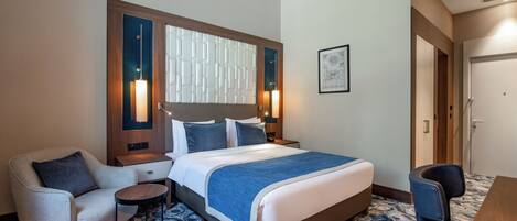 A hotel room with a large bed, a desk, a chair, and a small table.