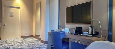 A hotel room with a large bed, a desk with a chair, a television, and a coffee maker.