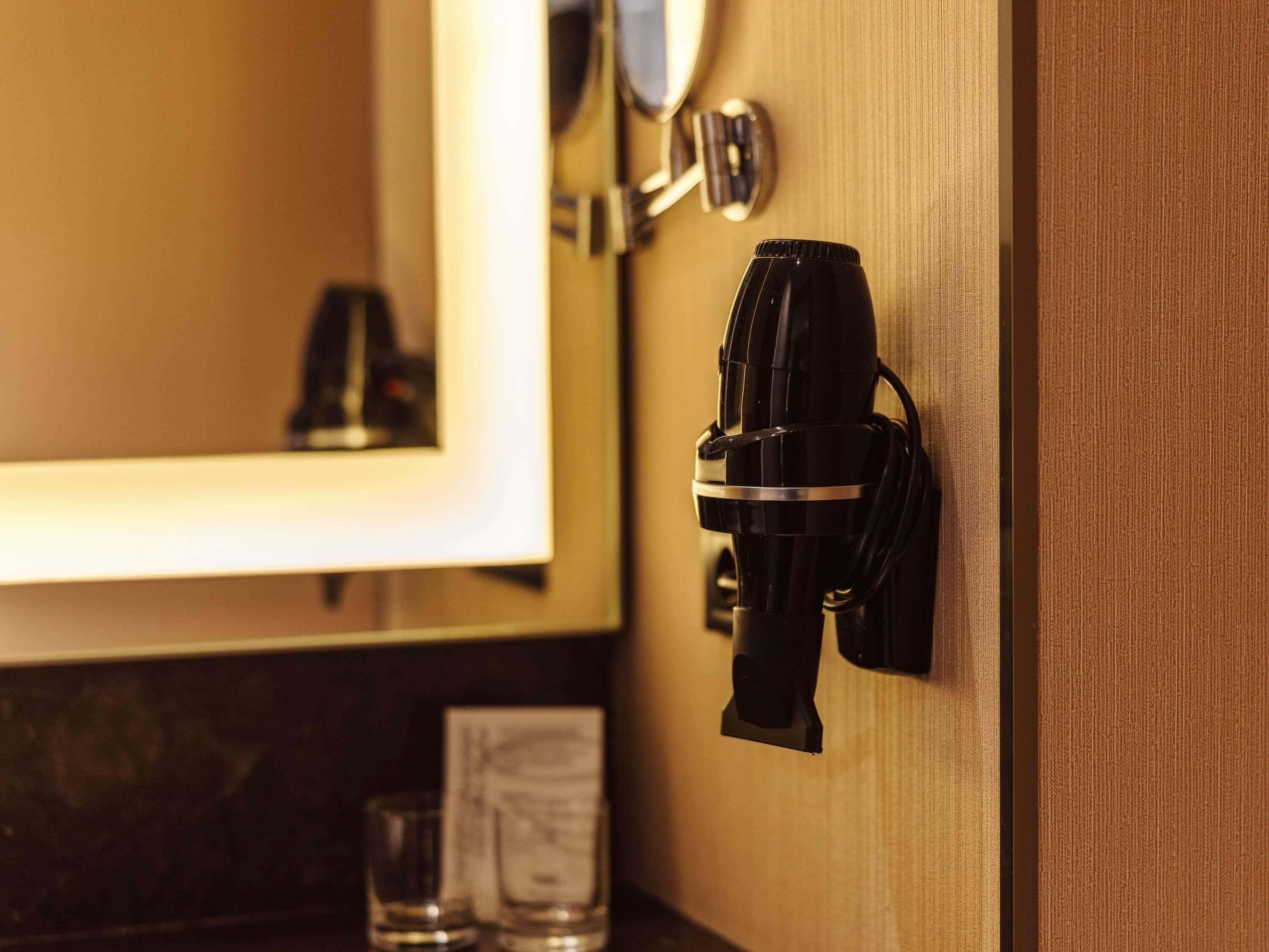A bathroom with a mirror, a sink, and a black hairdryer mounted on the wall.