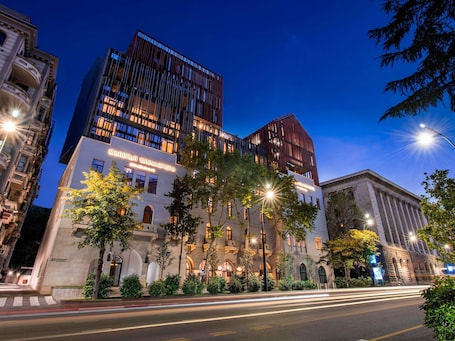 A hotel with a classical facade, modern upper floors, and a well-lit entrance.