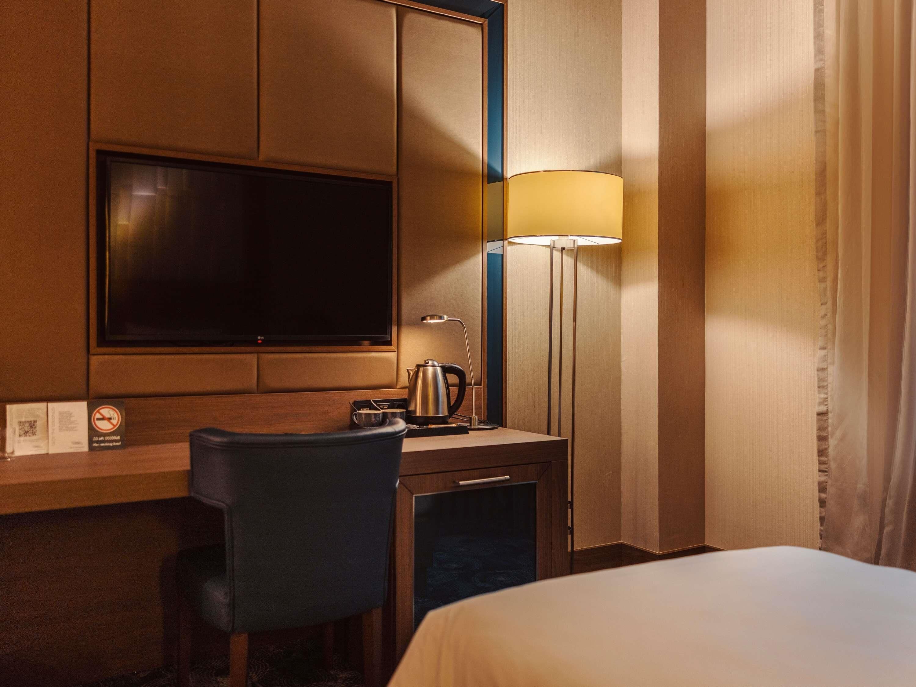 A hotel room with a bed, a desk with a chair, a television, a lamp, and a coffee maker.