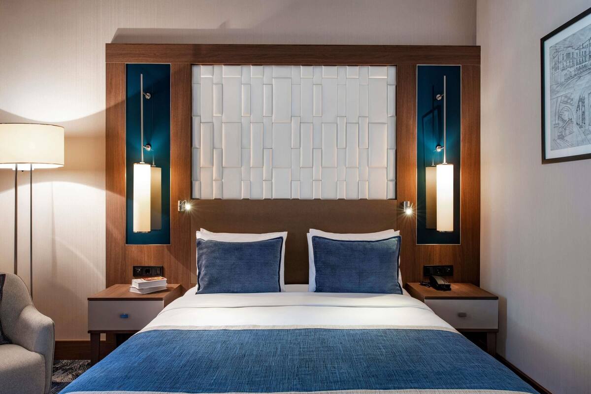 A hotel room with a large bed, two bedside tables, a nightstand, a lamp, and a framed picture on the wall.