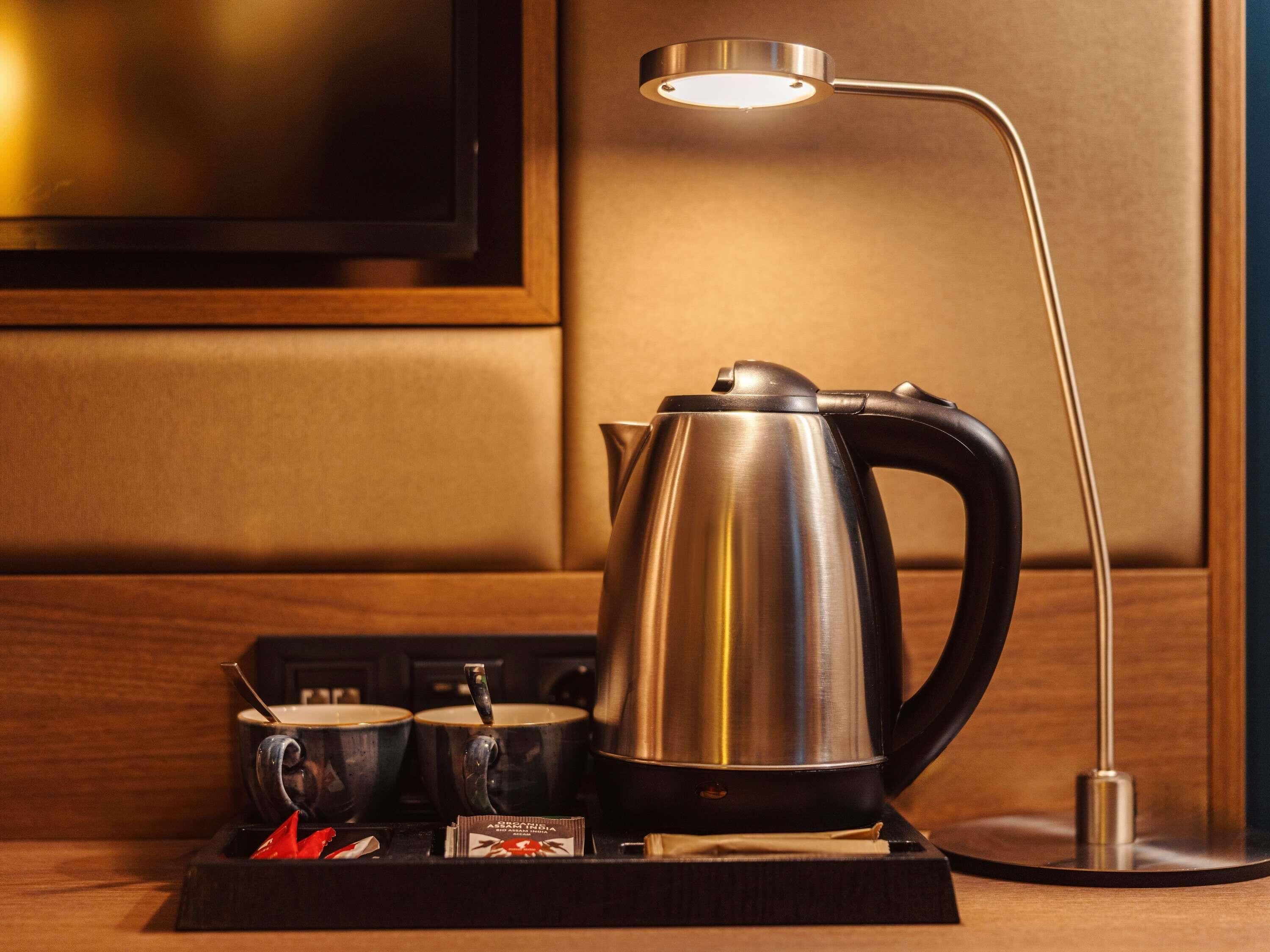 A hotel room with a modern coffee station featuring a kettle, cups, and a tray with tea bags.