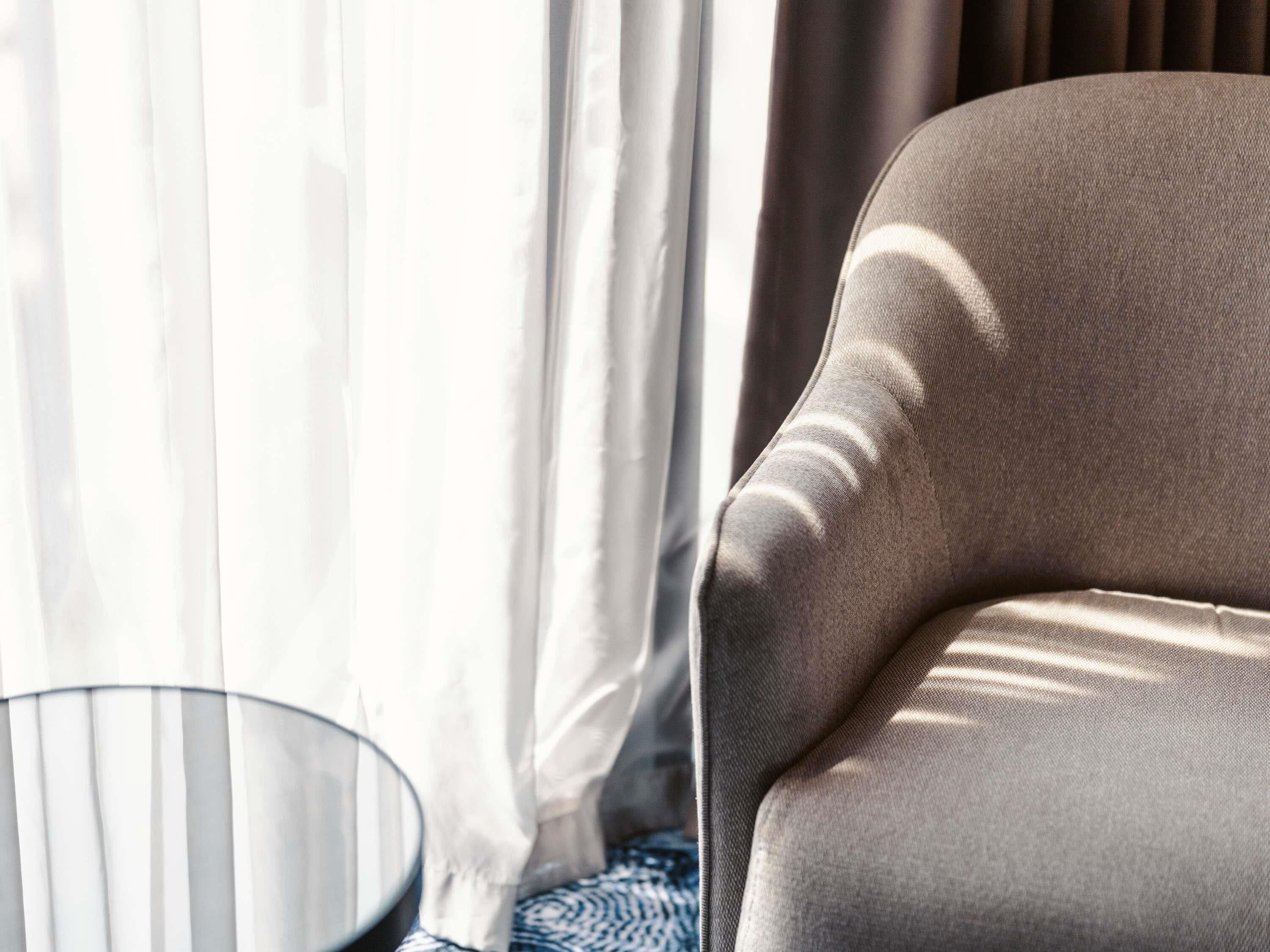 A room with a sofa, a round glass table, and sheer curtains.
