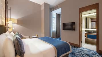 A hotel room with a bed, a TV, a desk, and a bathroom visible through an open door.