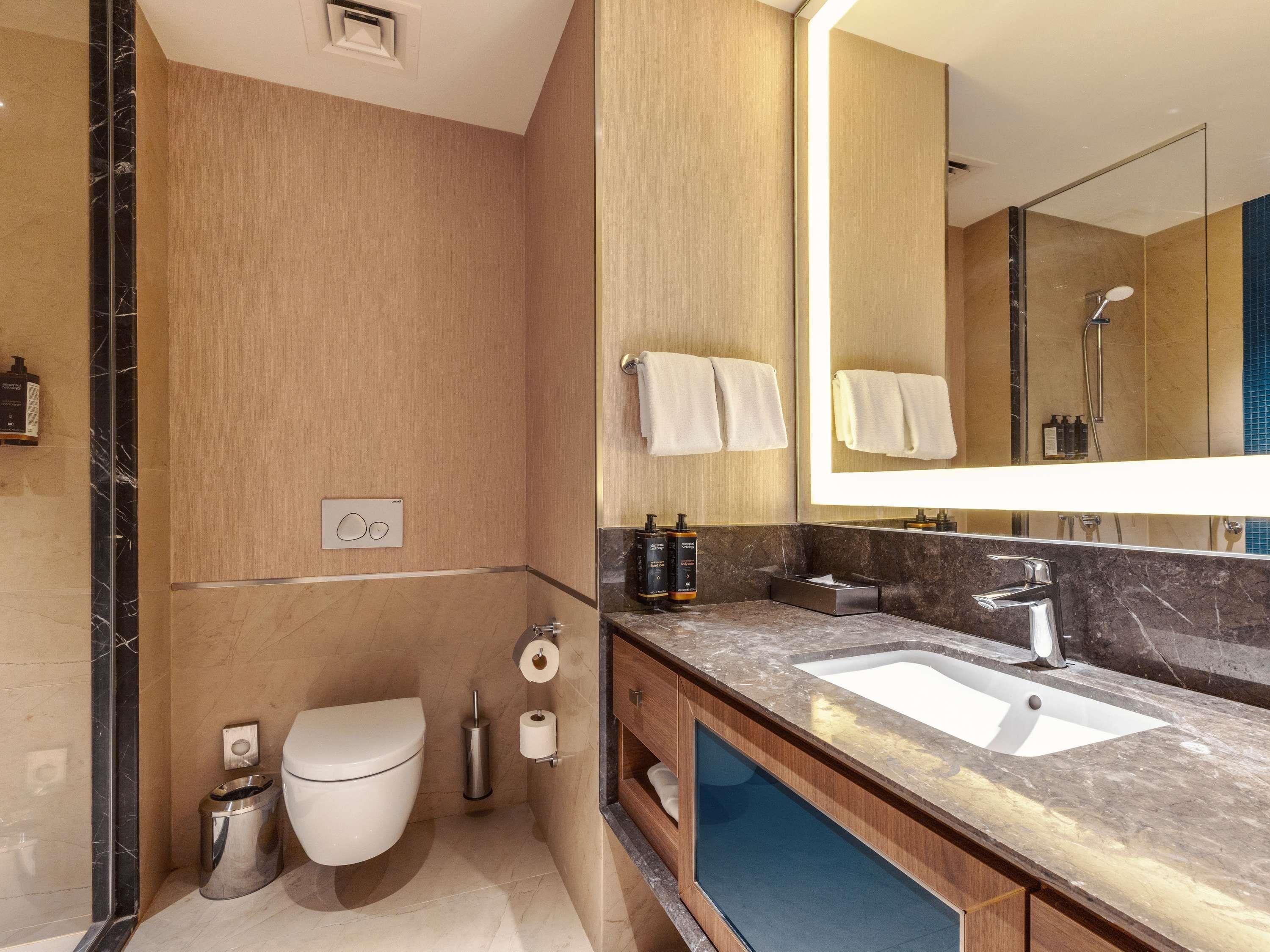 A modern bathroom with a marble sink, a toilet, a bidet, and a large mirror.