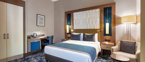 A hotel room with a large bed, a desk with a lamp, a chair, and a wardrobe.