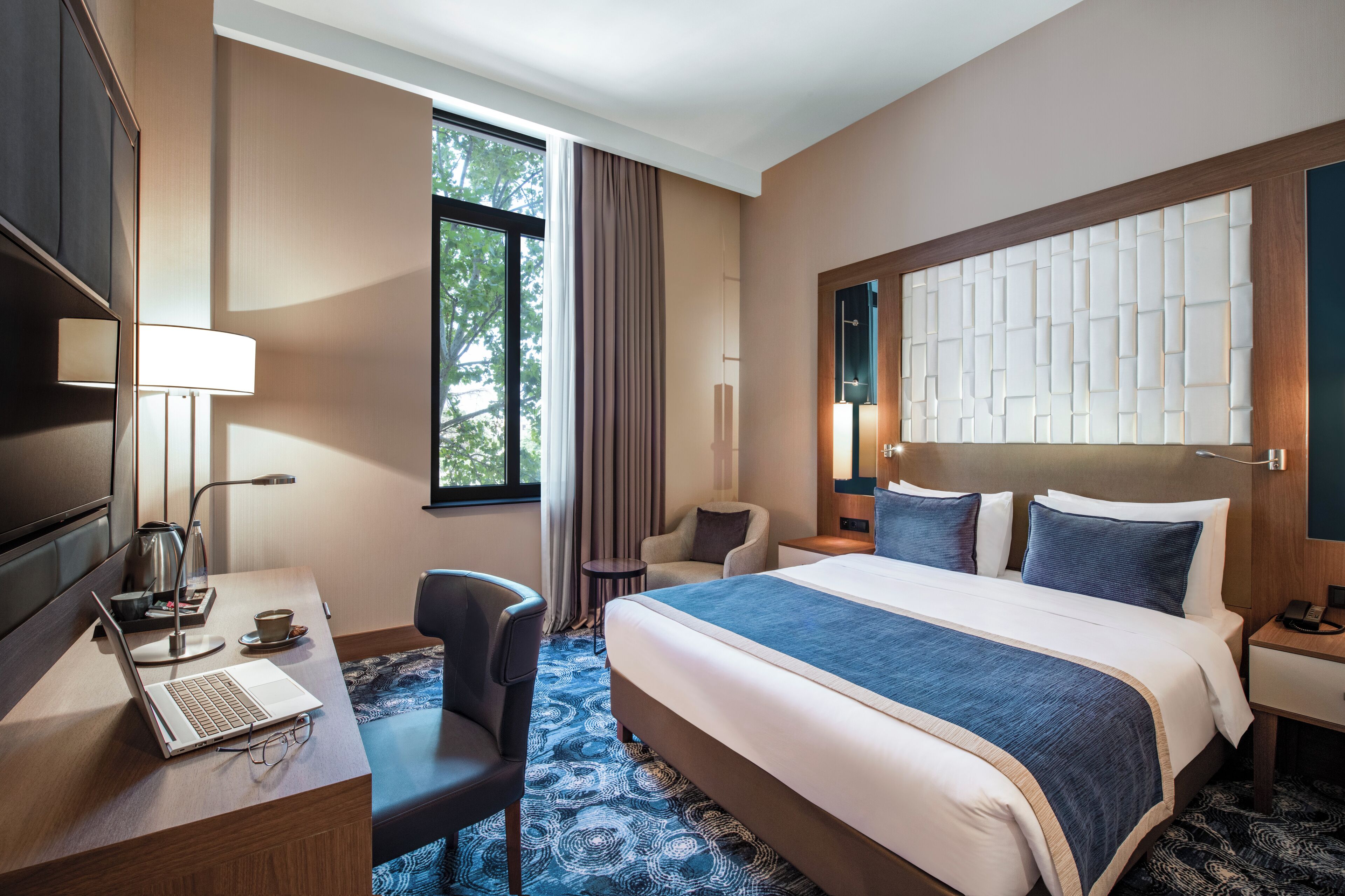 Une chambre d’hôtel avec un lit, un bureau, une chaise et une grande fenêtre.