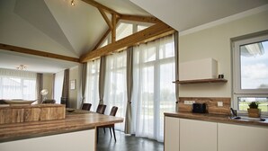 A modern kitchen with wooden beams, a dining area with chairs, and a large window providing natural light. - Die Ausstattung vom Ferienhaus Bauernrose (Vaschwitz)