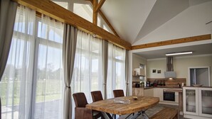 A spacious kitchen with a wooden table and chairs, a bench, and a view of the outdoors through large windows. - Die Ausstattung vom Ferienhaus Bauernrose (Vaschwitz)