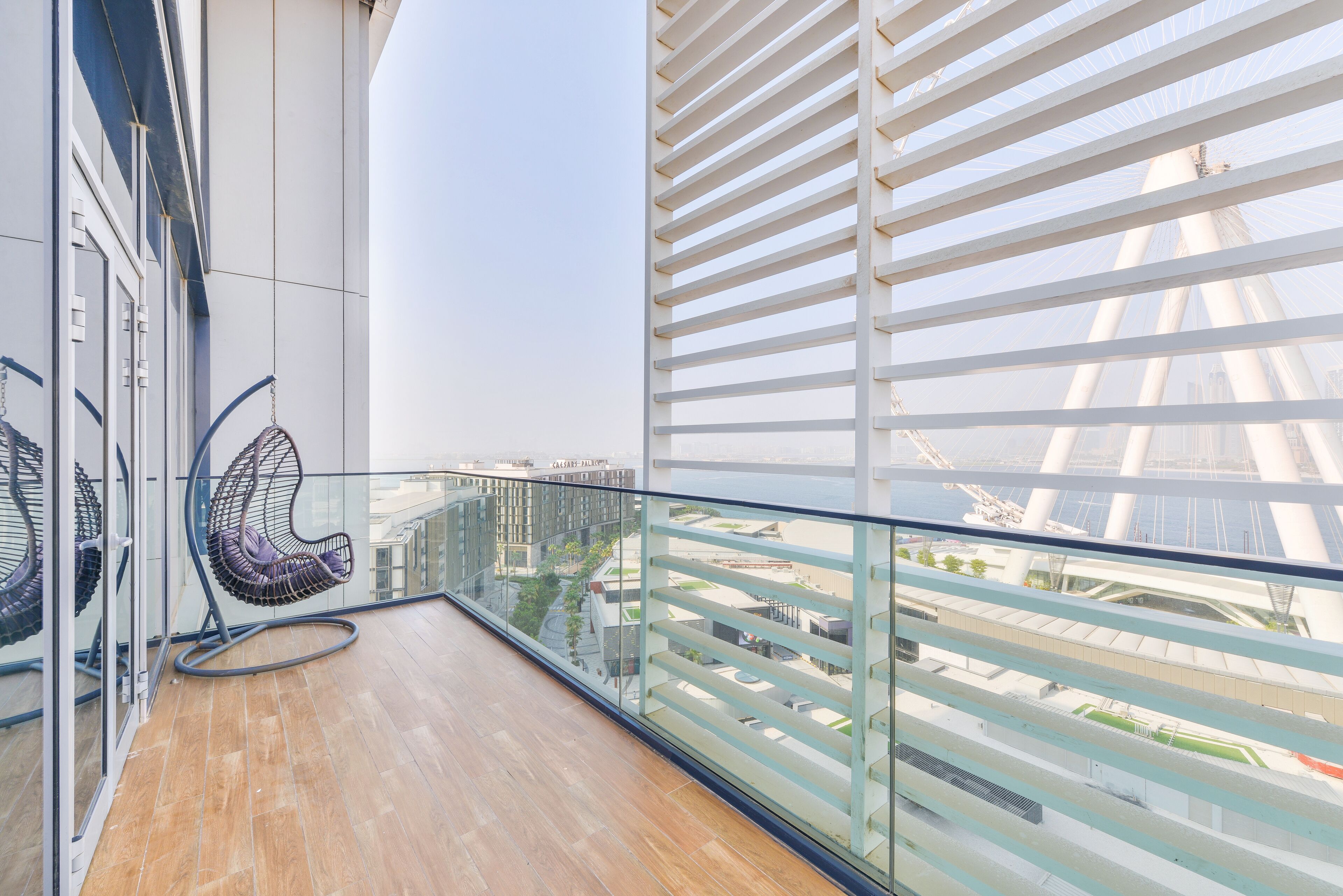 A balcony with a hanging chair, glass railings, and a view of a bridge.