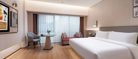 Habitación de hotel con una cama grande, un escritorio con una silla, una mesita con un florero y una ventana con cortinas.