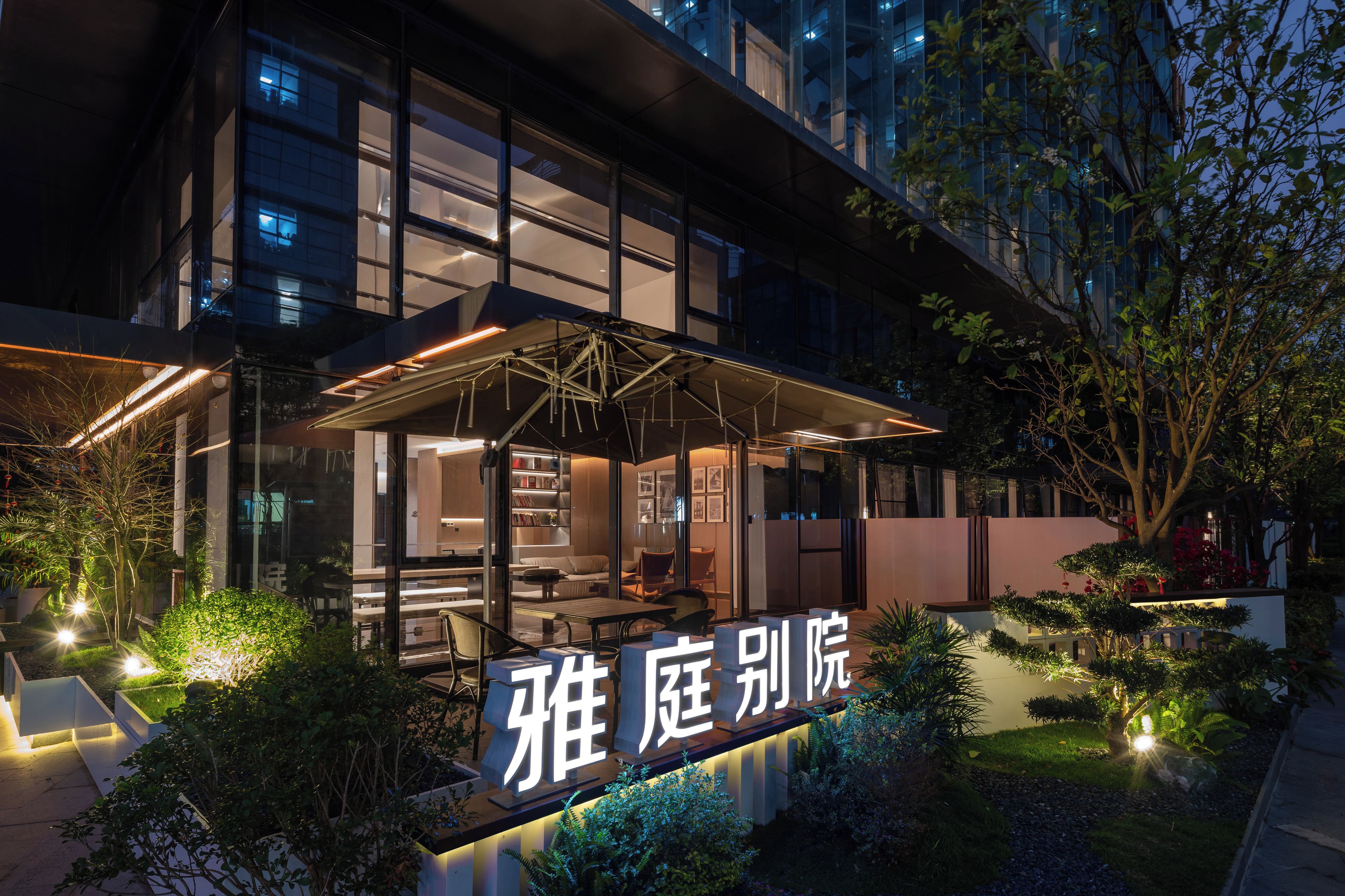 A modern building with a glass facade, outdoor seating area, and a sign with Chinese characters.