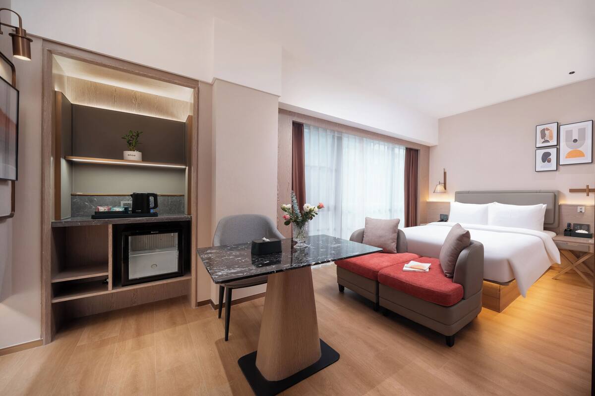 Ett modernt hotellrum med en säng, en soffa, ett matbord och ett litet kök.