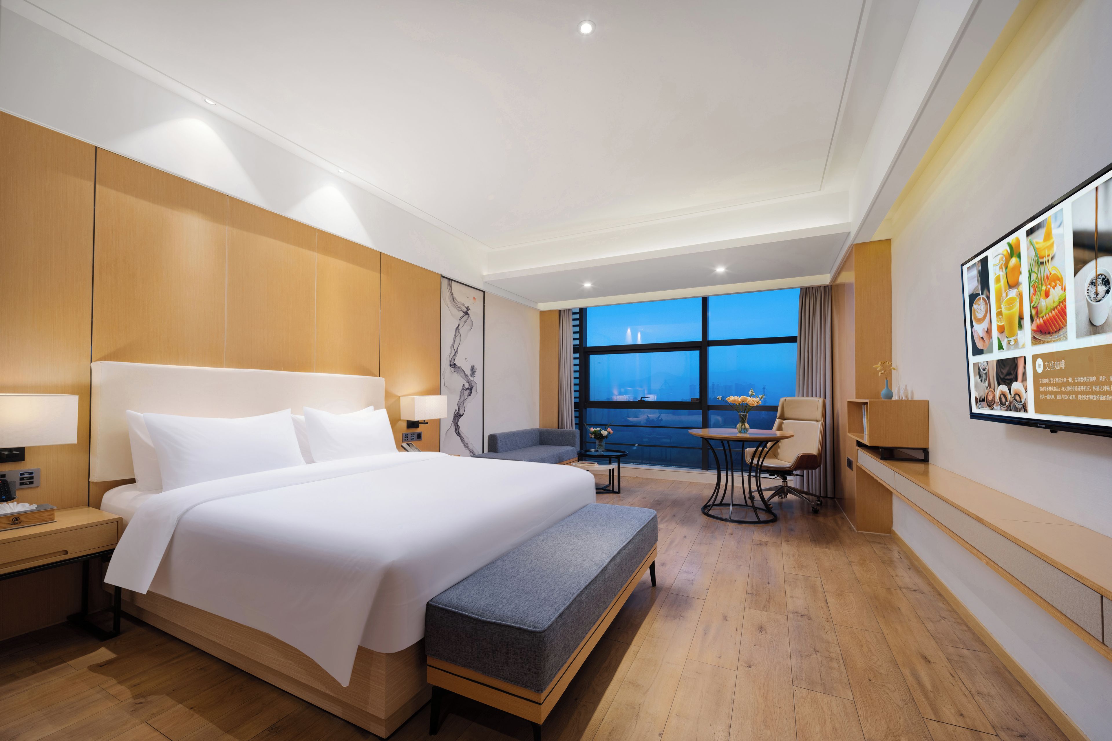 Habitación de hotel con una cama grande, un escritorio, una silla y vistas a la ciudad a través de la ventana.