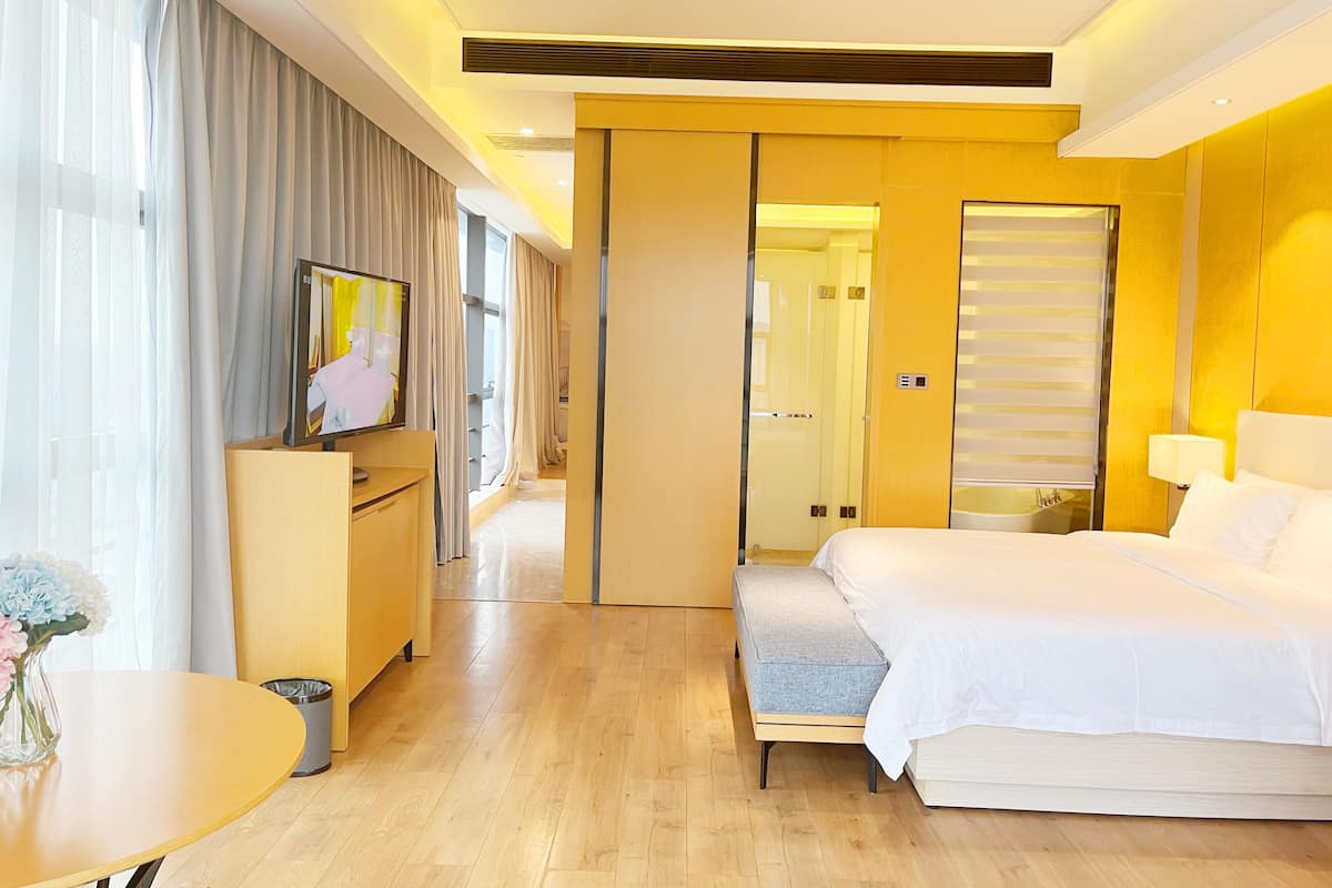 Ett modernt hotellrum med en säng, ett nattduksbord, en TV och utsikt över korridoren.