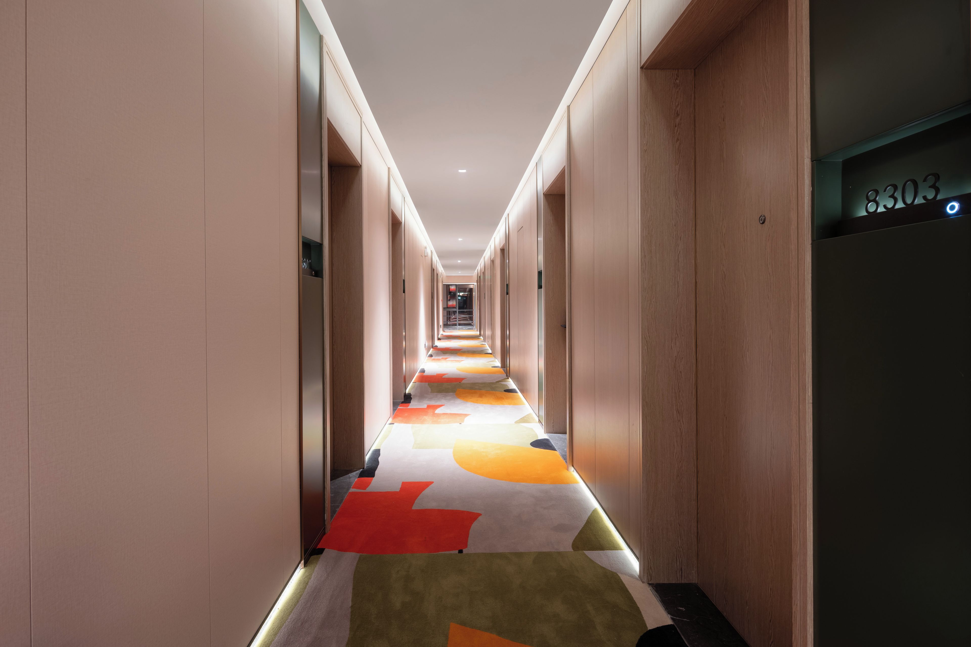 A hotel corridor with a carpeted floor, wooden walls, and a visible elevator with the number 8303.