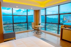 A hotel room with large windows, a bed, a desk, and a chair.