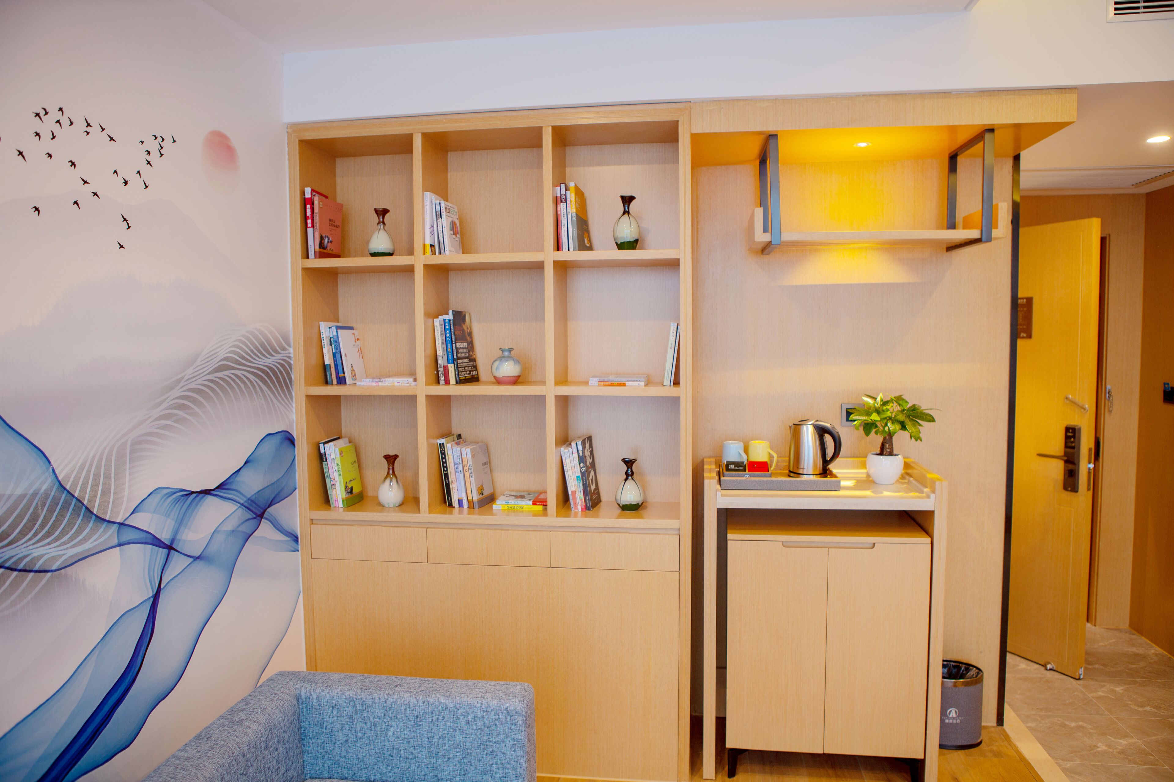 A modern room with a built-in bookshelf, a small kitchenette, and a wall mural.