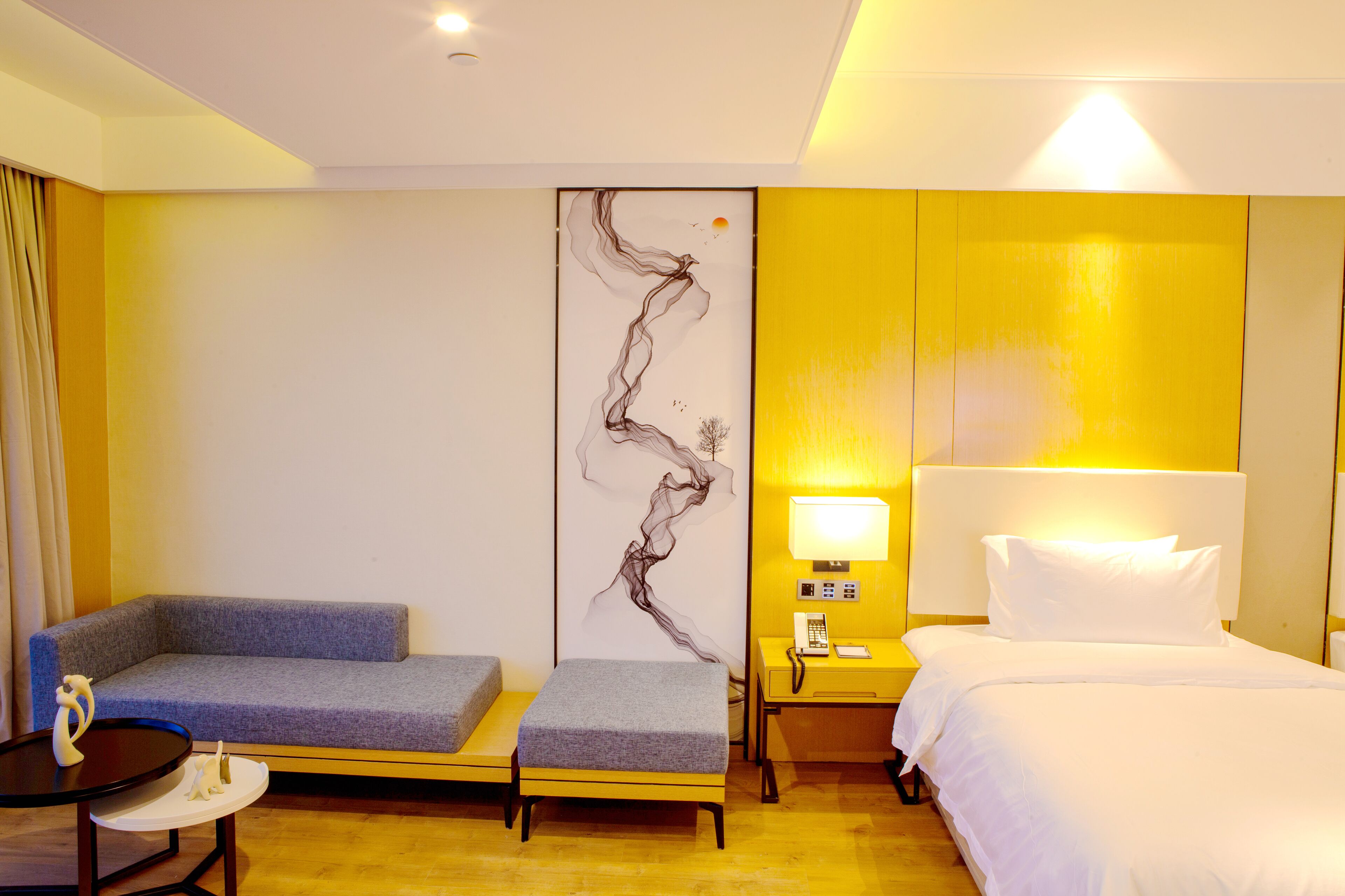 A hotel room with a bed, a sofa, a small table, and a wall art piece.