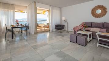 Una sala moderna con un sofá gris, un comedor con mesa dispuesta para dos personas, y un balcón con vista a la ciudad.
