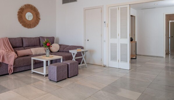 Una sala de estar moderna con un sofá, una mesa de centro y una mesita auxiliar. Hay una puerta con contraventanas y un espejo en la pared.