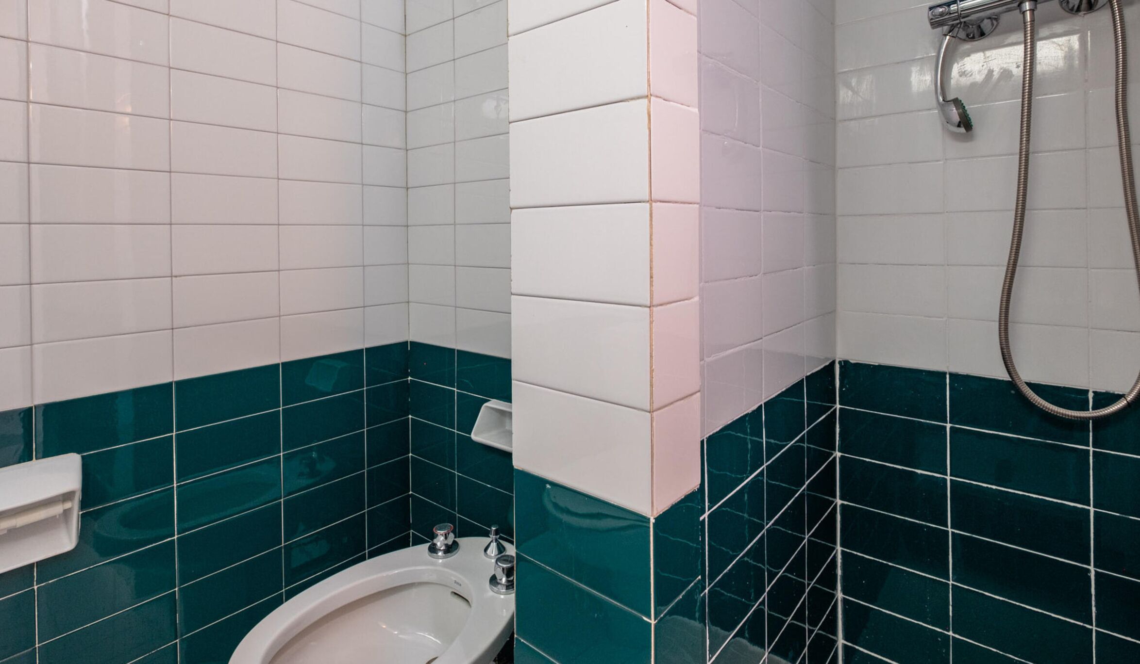 Een badkamer met witte en teal tegels, een toilet en een douche met een douchekop.