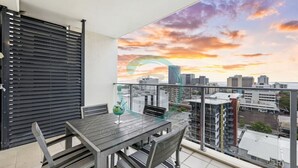 Un balcon avec une table et des chaises, offrant une vue sur le paysage urbain au coucher du soleil.