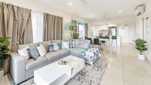 Un salon moderne avec un canapé gris, une table basse et, au fond, un coin repas.