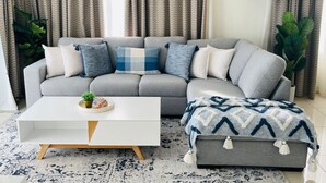 Un salon avec un canapé gris, une table basse blanche et des rideaux à motifs.