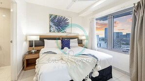 Une chambre d’hôtel moderne dotée d’un grand lit, d’une table de chevet, d’un ventilateur de plafond et d’une fenêtre donnant sur la ville.