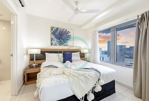 Une chambre d’hôtel moderne dotée d’un grand lit, d’une table de chevet, d’un ventilateur de plafond et d’une fenêtre donnant sur la ville.