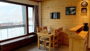 Une pièce chaleureuse avec un décor intérieur en bois, une table à manger avec des chaises, un banc, un téléviseur fixé au mur et une machine à café.
