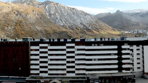 Un bâtiment moderne à la façade noire et blanche, situé dans une région montagneuse où l’on peut apercevoir des infrastructures et où le ciel est dégagé.