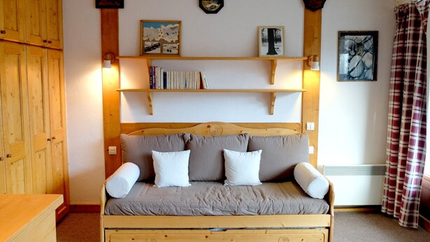 Une pièce chaleureuse avec un lit en bois, un canapé-lit, des étagères en bois remplies de livres et une horloge murale.
