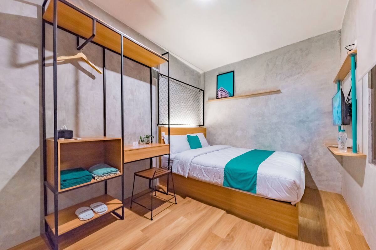 A modern bedroom with a bed, wooden shelves, a desk, and a hanging chair.