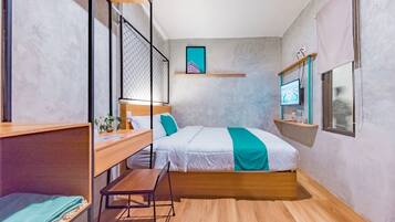 A compact bedroom with a bed, a desk, and a small seating area.