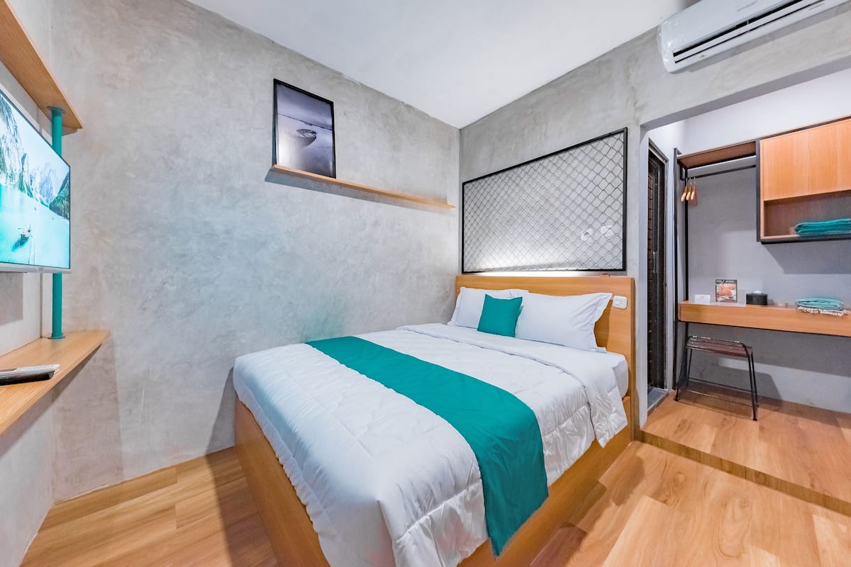 A modern hotel room with a bed, a desk, a chair, a TV, and a wardrobe.