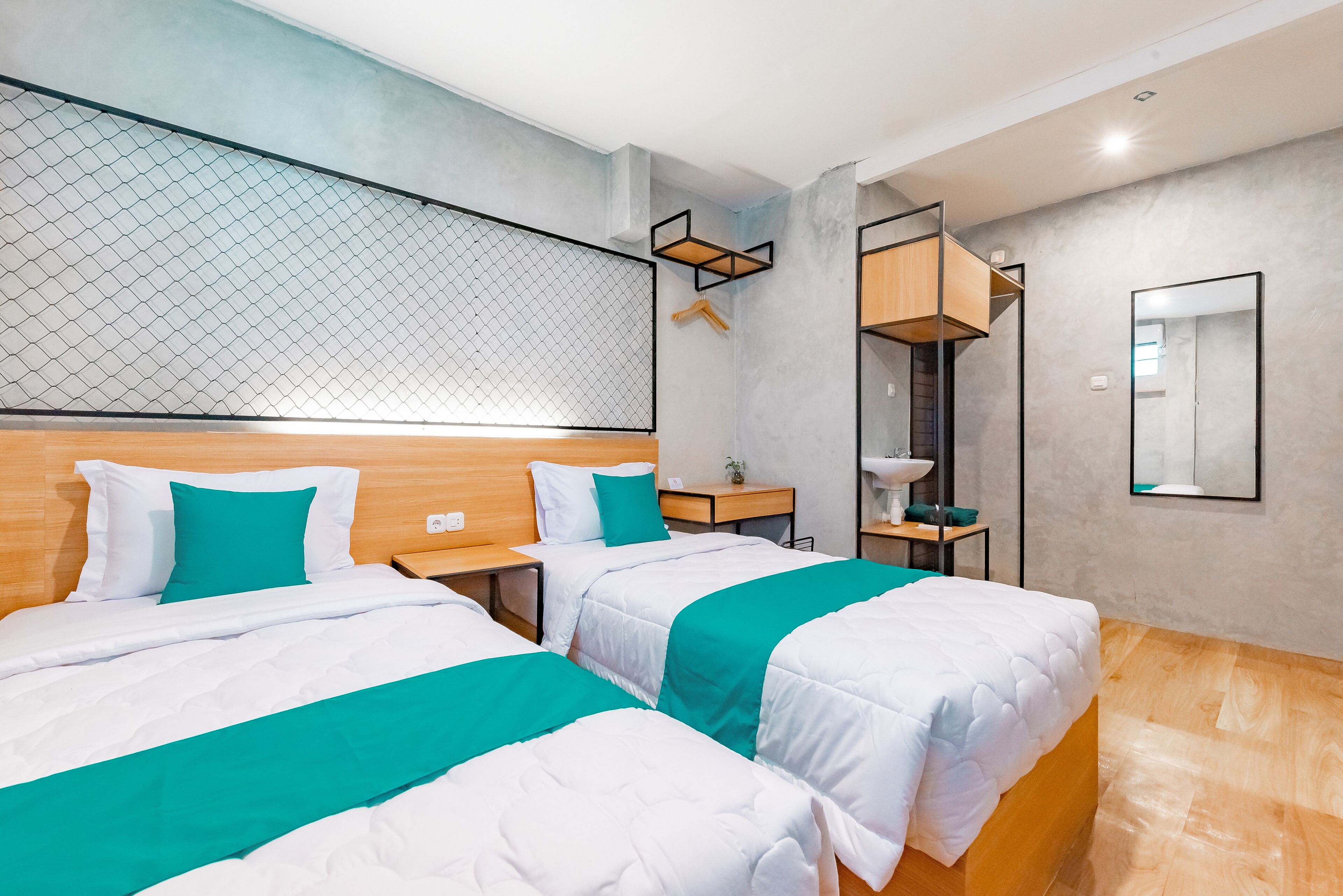 A modern hotel room with two beds, a large mirror, a small table, and a wall-mounted shelf.
