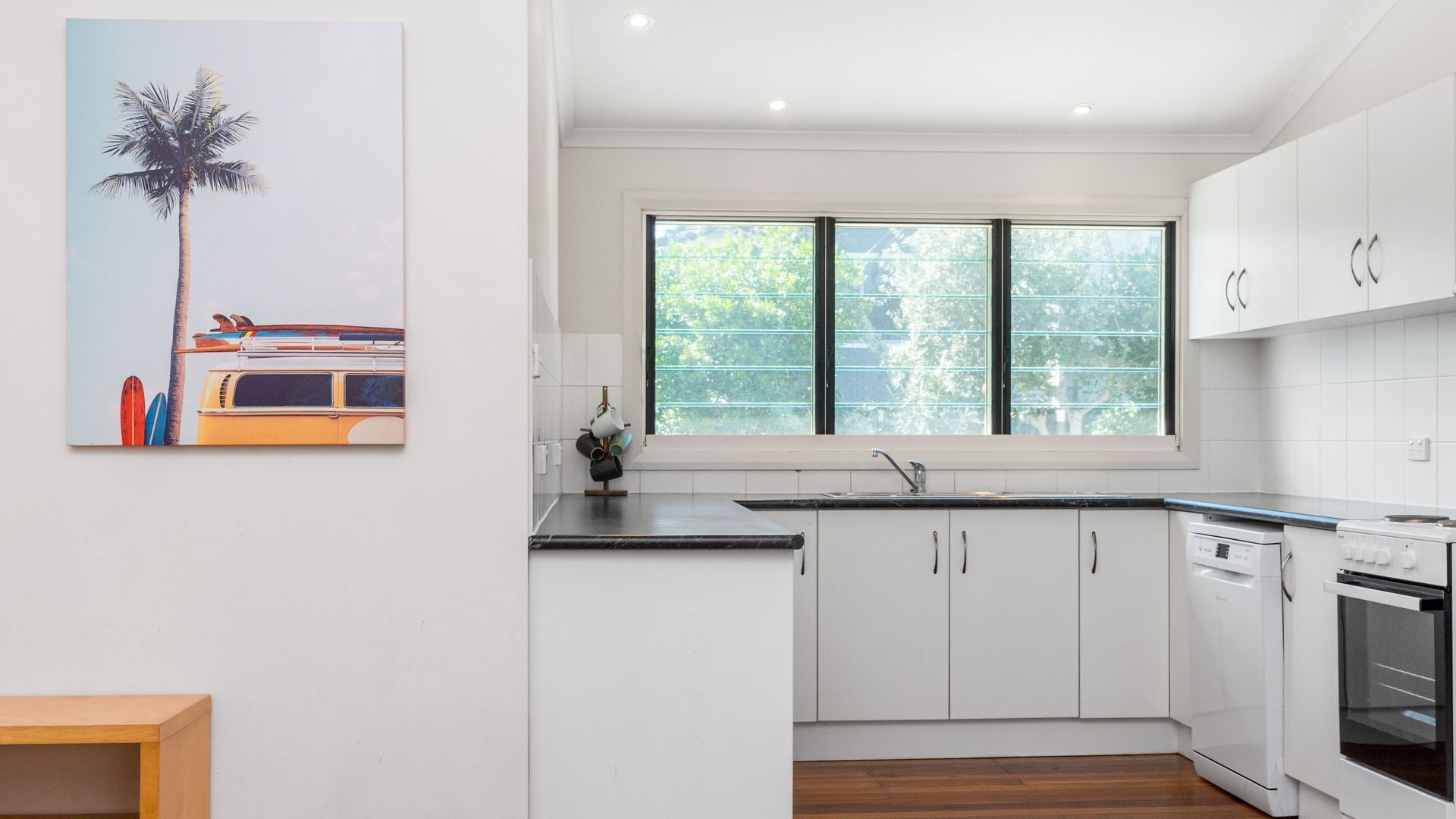 A modern kitchen with white cabinets, a black countertop, and a large window with a view of trees.