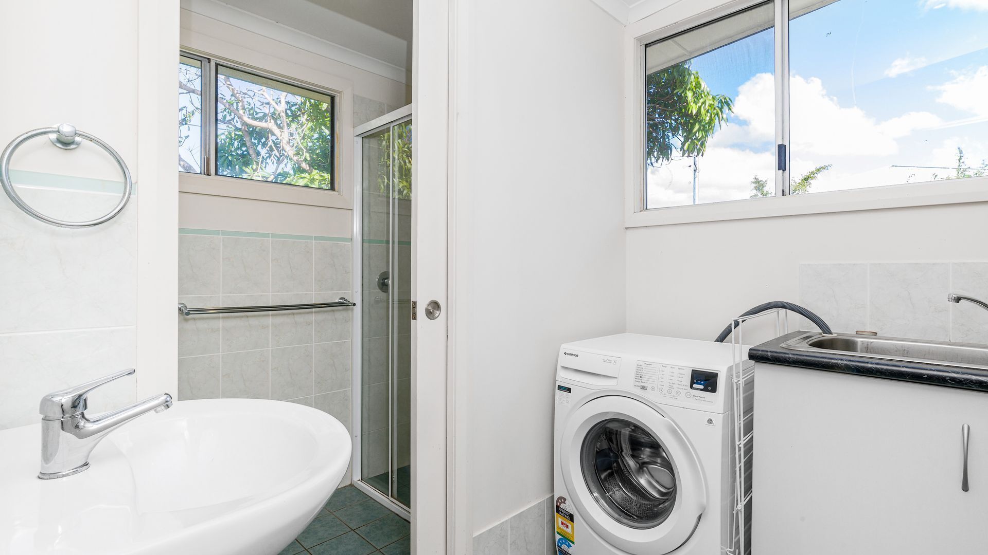 Een kleine badkamer met een wastafel, een wasmachine en een douchecabine van glas.