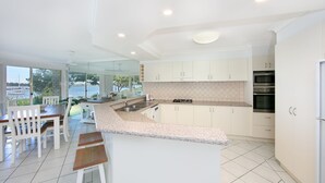 A modern kitchen with white cabinets, a granite countertop, and a view of the outdoors. - River Luxury - Set right on Iluka Bay (Iluka)